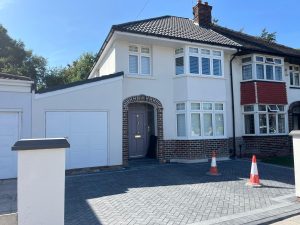The same house after renovation: smooth white render, new grey tiled roof, new windows, brick-arched porch and a new block-paved driveway