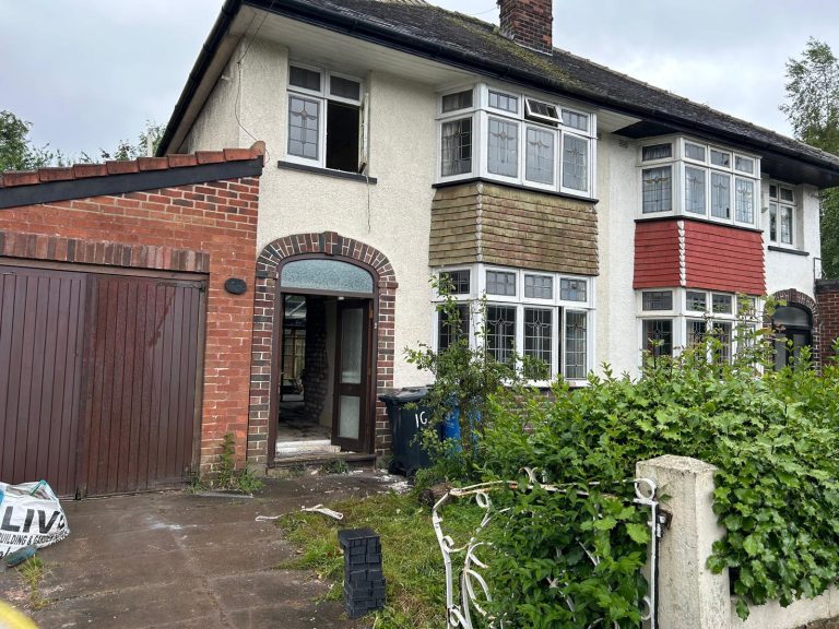 The house before renovation: tired pebbledash render, moss-covered roof, overgrown front garden and an open doorway during strip-out
