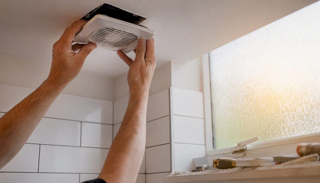 Hands installing extractor fan in utility room