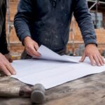 Builder's hands with architectural plans on site