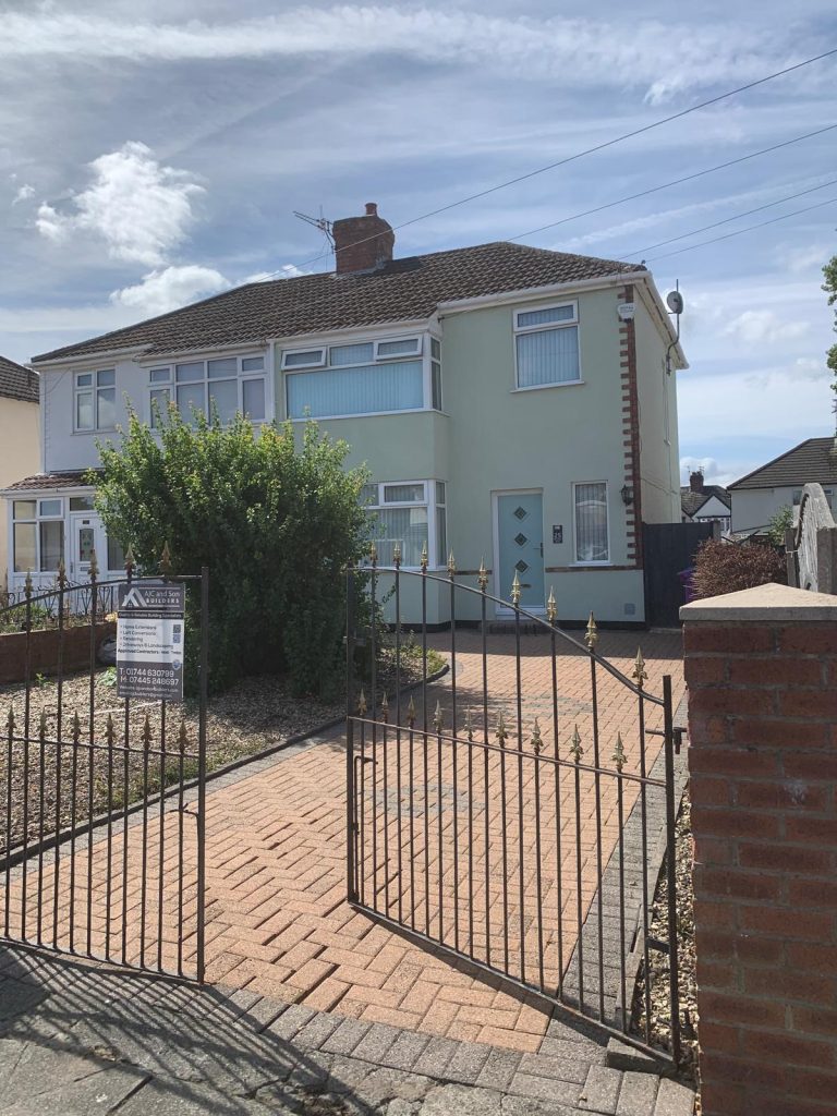 Semi-detached house newly rendered in pale green with a red brick plinth, white windows and a block-paved driveway, AJC and Son Builders board by the gate