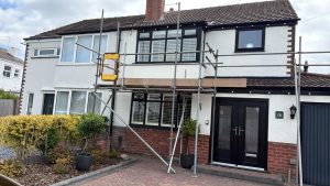Close view of the newly rendered white front elevation with red brick plinth and scaffolding still in place