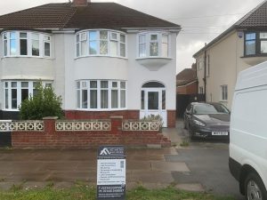 Semi-detached house rendered in smooth white with a red brick plinth and white bay windows, AJC and Son Builders sign board on the front path