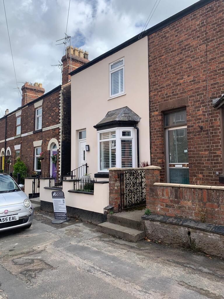 Terraced house front rendered in smooth cream with a black bay window canopy, white door and railings, AJC and Son Builders sign board outside
